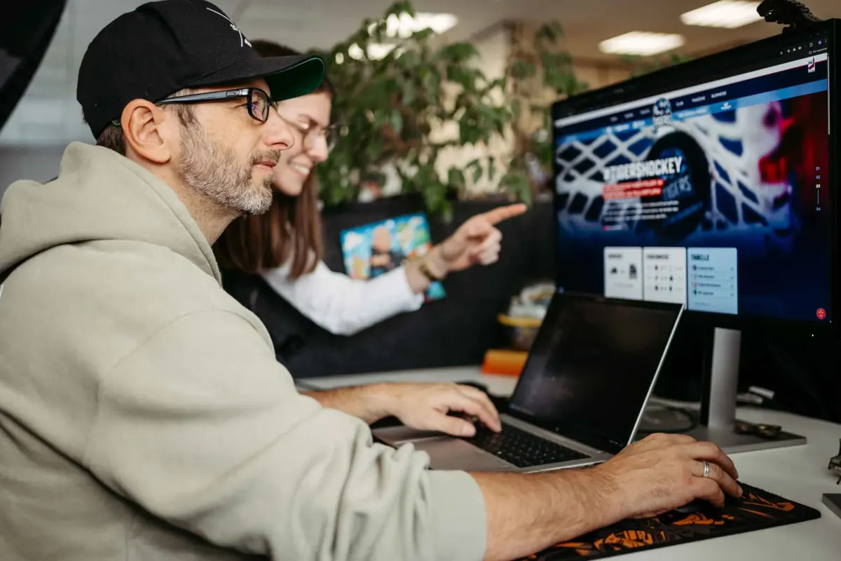 Zwei danubius-Mitarbeiter besprechen die Website der Straubing Tigers am Bildschirm
